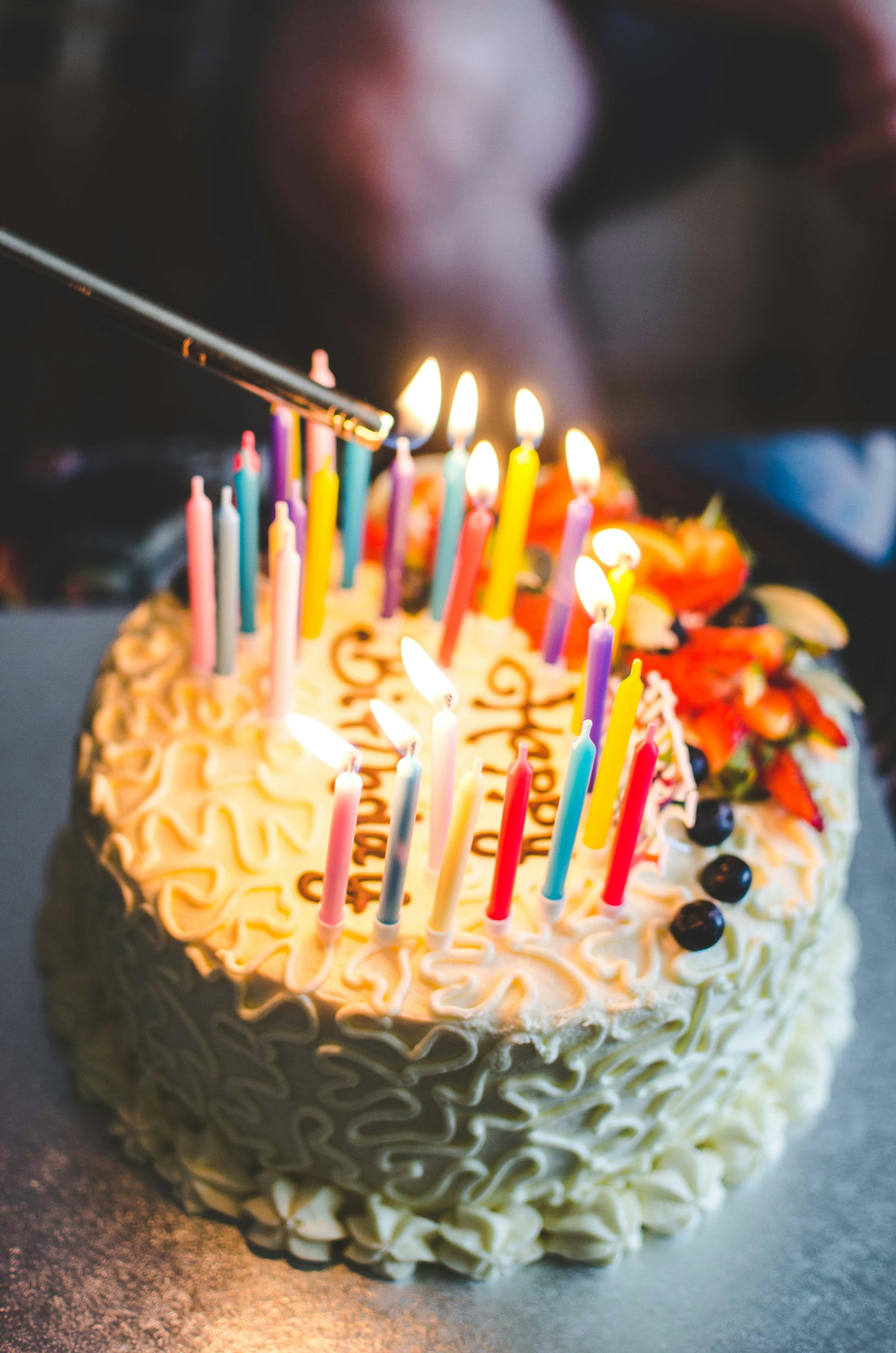Candles being lit on a birthday cake with white frosting and berries